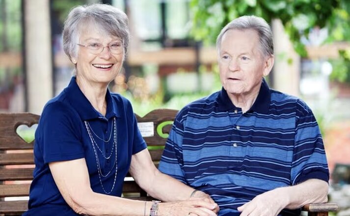elder couple both wearing blue shirts sitting on a bench on the memory care campus in louisville ky
