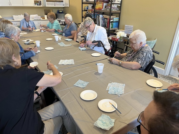 A group of seniors at Traditions at Beaumont is sitting around a gray table, working on an art project with white plates and green patterned napkins at a senior living community.