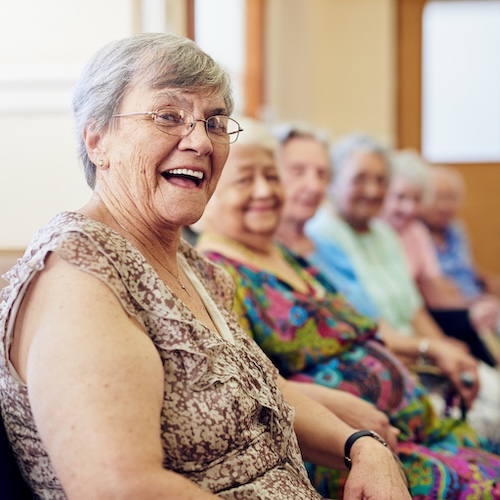 Portrait of a smiling senior woman sitting with others in assisted living facility.
